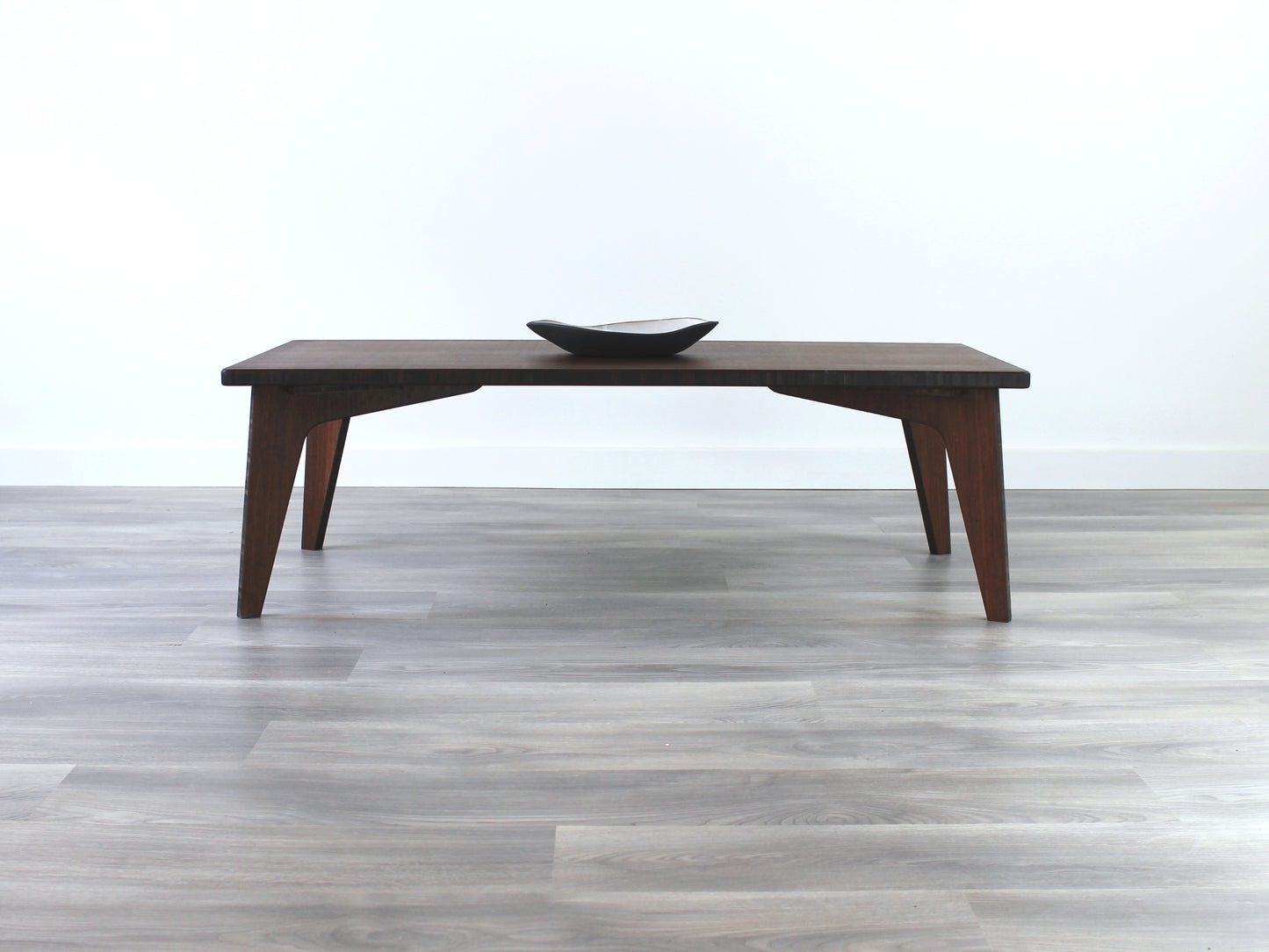 A rectangular low table made of bamboo with a walnut finish, placed on a grey floor, designed for multi-functional use in living spaces. Small black pottery vessel on table top. 

japanese furniture
japanese low table
low coffee table
low dining table
low table
mid century
minimalist
minimalist table
modern