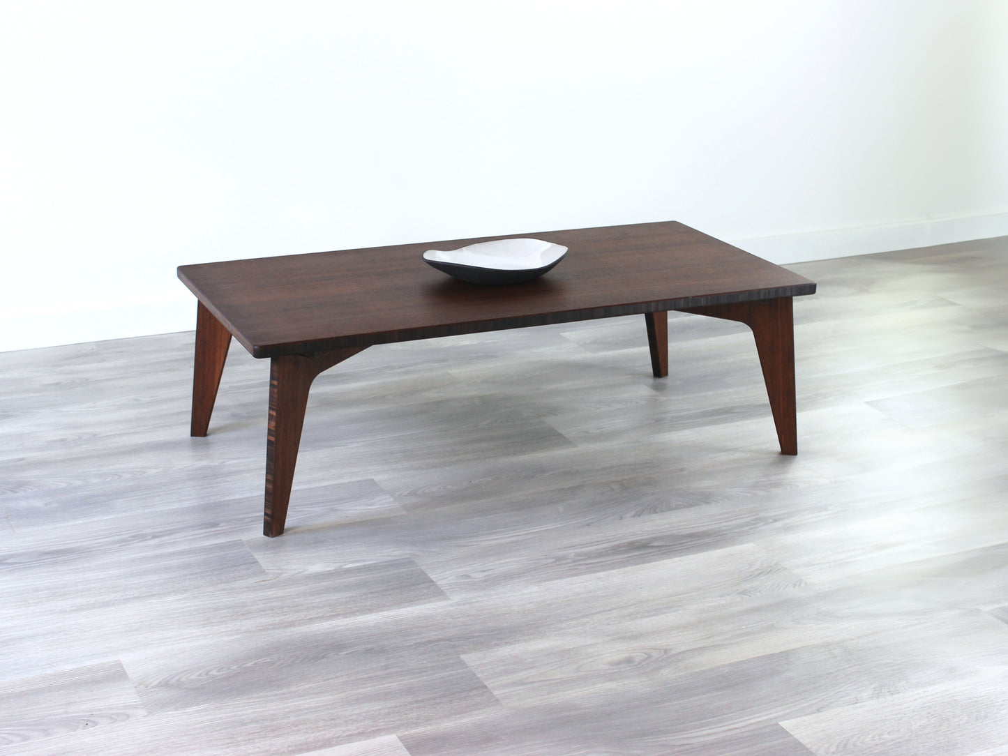 A rectangular low table made of bamboo with a walnut finish, placed on a grey floor, designed for multi-functional use in living spaces. Small black pottery vessel on table top. 

japanese furniture
japanese low table
low coffee table
low dining table
low table
mid century
minimalist
minimalist table
modern