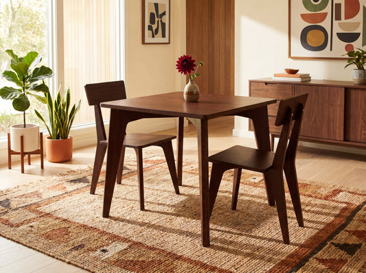 Dining room with bamboo table and chairs on a patterned rug, plants, and artwork.