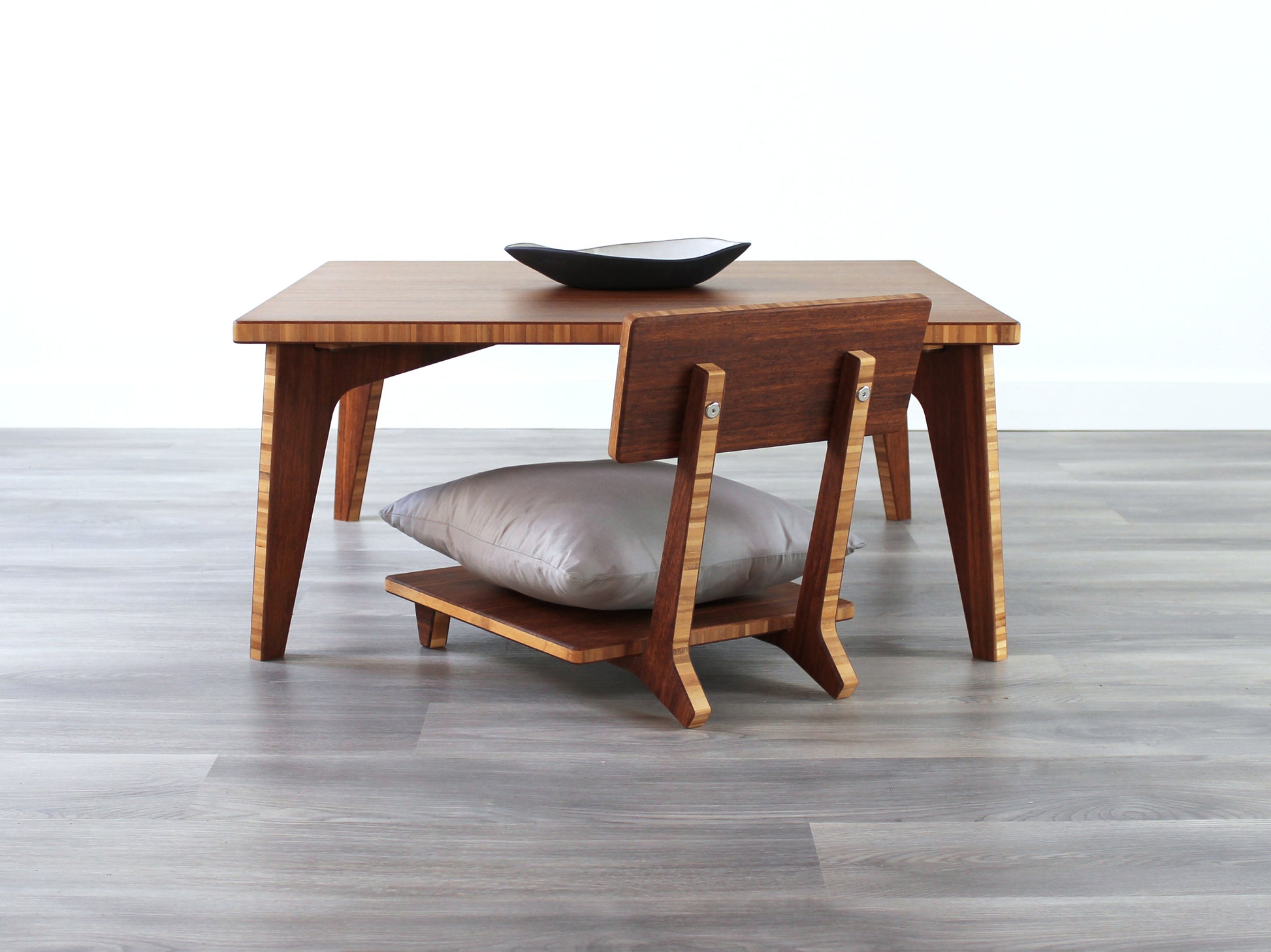 Small Square Table Set in chestnut finish. A Floor Chair Comfort is placed below. A small black pottery vessel is placed on top of the table. 

sustainable bamboo, renewable bamboo, solid bamboo, eco-friendly furniture, zero-waste, carbon neutral, natural materials, natural-based finish, repairable furniture