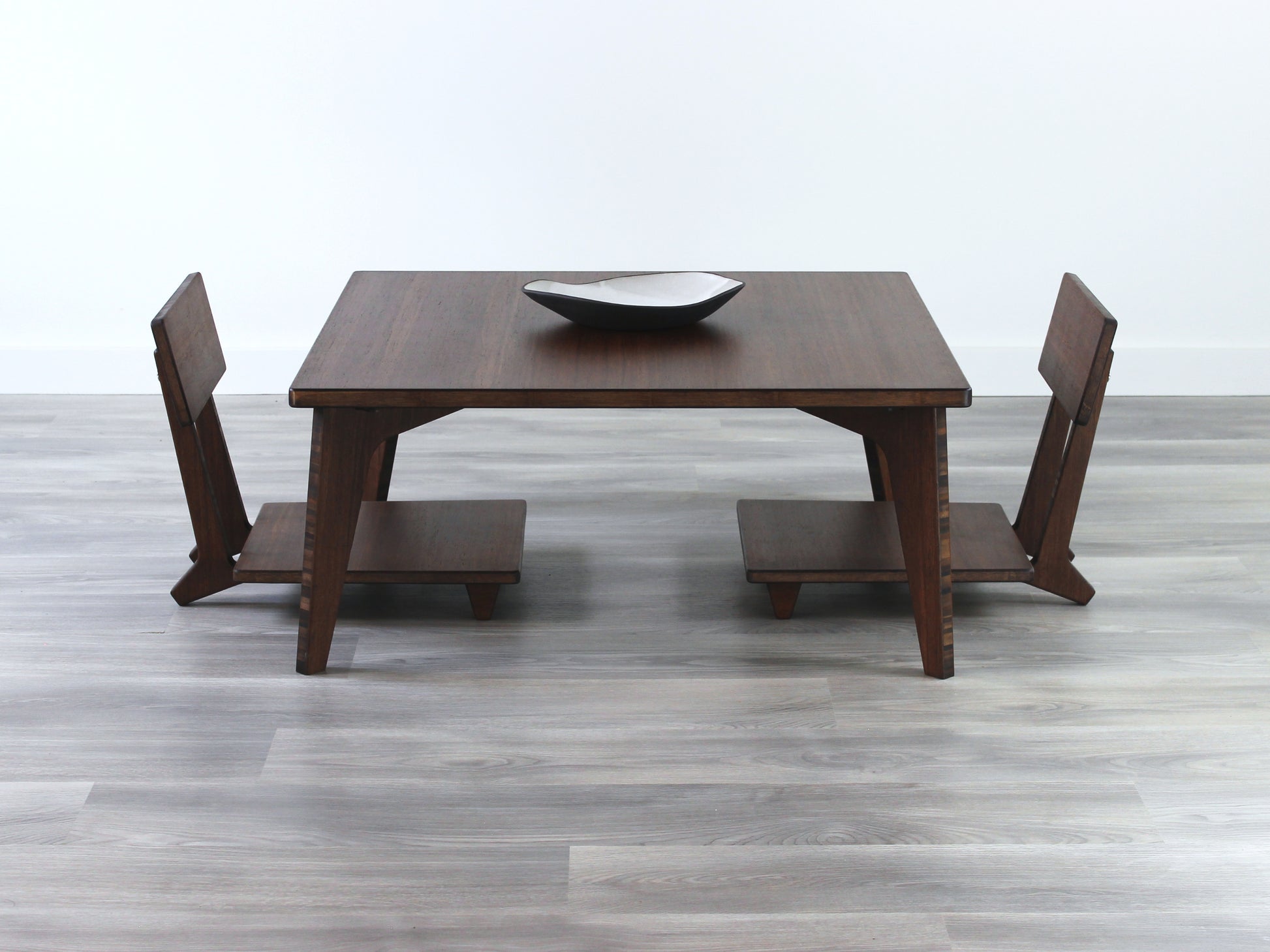 Small Square Table Set in walnut finish. Two Floor Chair Comfort are placed below. A small black pottery vessel is placed on top of the table. 

sustainable bamboo, renewable bamboo, solid bamboo, eco-friendly furniture, zero-waste, carbon neutral, natural materials, natural-based finish, repairable furniture