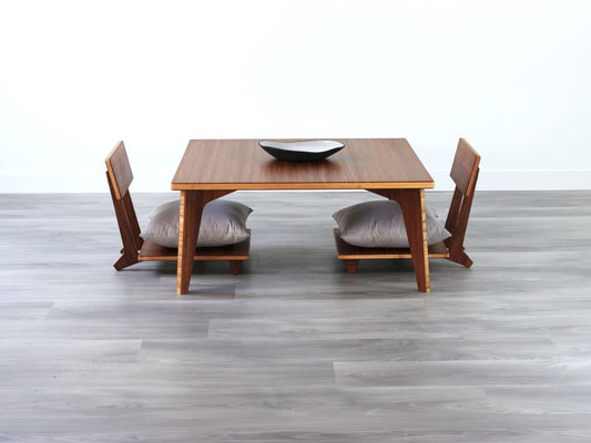 Small Square Table Set in chestnut finish. Two Floor Chair Comfort with grey pillows are placed below. A small black pottery vessel is placed on top of the table. 

sustainable bamboo, renewable bamboo, solid bamboo, eco-friendly furniture, zero-waste, carbon neutral, natural materials, natural-based finish, repairable furniture