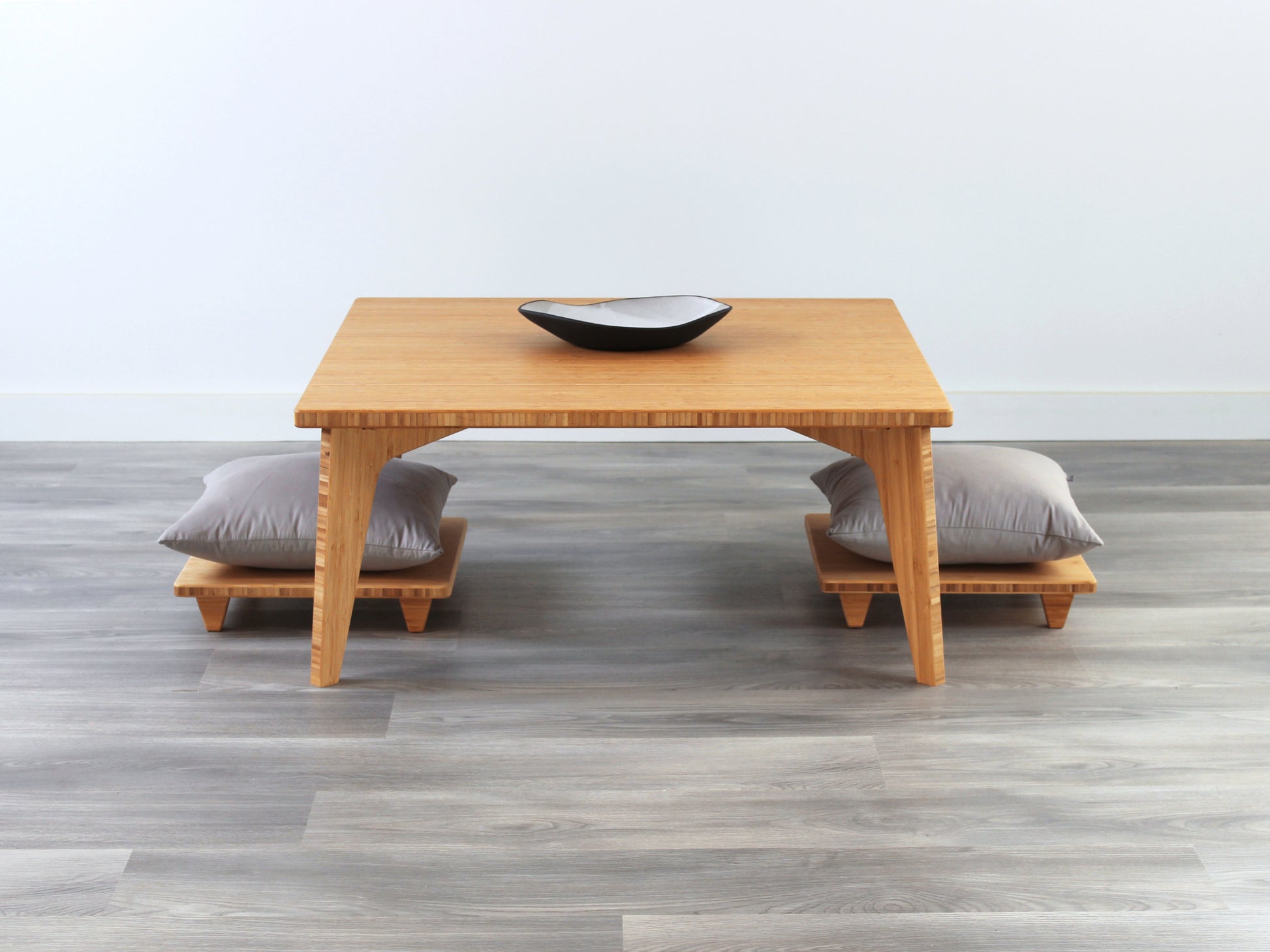Small Square Table Set in natural finish. Two Floor Chair Posture with grey pillows are placed below. A small black pottery vessel is placed on top of the table. 

sustainable bamboo, renewable bamboo, solid bamboo, eco-friendly furniture, zero-waste, carbon neutral, natural materials, natural-based finish, repairable furniture