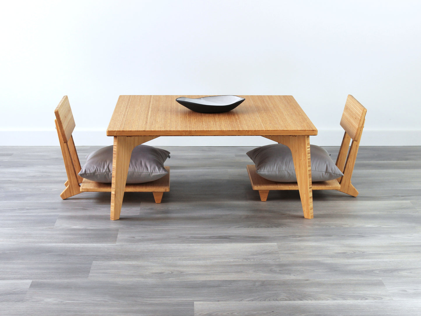 Small Square Table Set in natural finish. Two Floor Chair Comfort with grey pillows are placed below. A small black pottery vessel is placed on top of the table. 

sustainable bamboo, renewable bamboo, solid bamboo, eco-friendly furniture, zero-waste, carbon neutral, natural materials, natural-based finish, repairable furniture