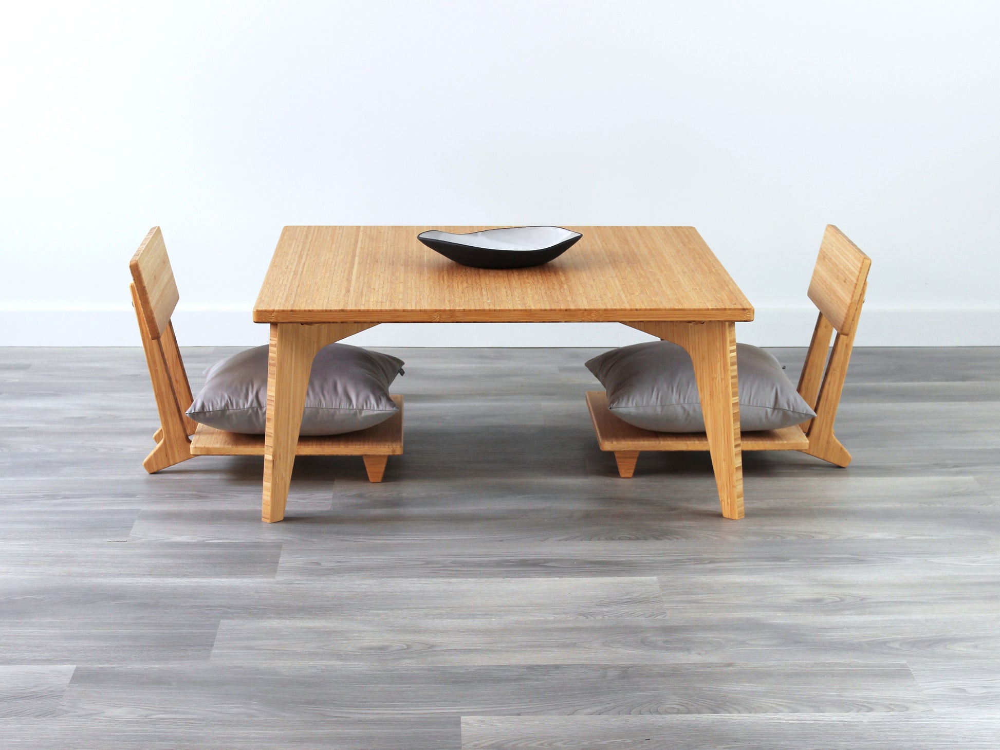 Small Square Table Set in natural finish. Two Floor Chair Comfort with grey pillows are placed below. A small black pottery vessel is placed on top of the table. 

sustainable bamboo, renewable bamboo, solid bamboo, eco-friendly furniture, zero-waste, carbon neutral, natural materials, natural-based finish, repairable furniture