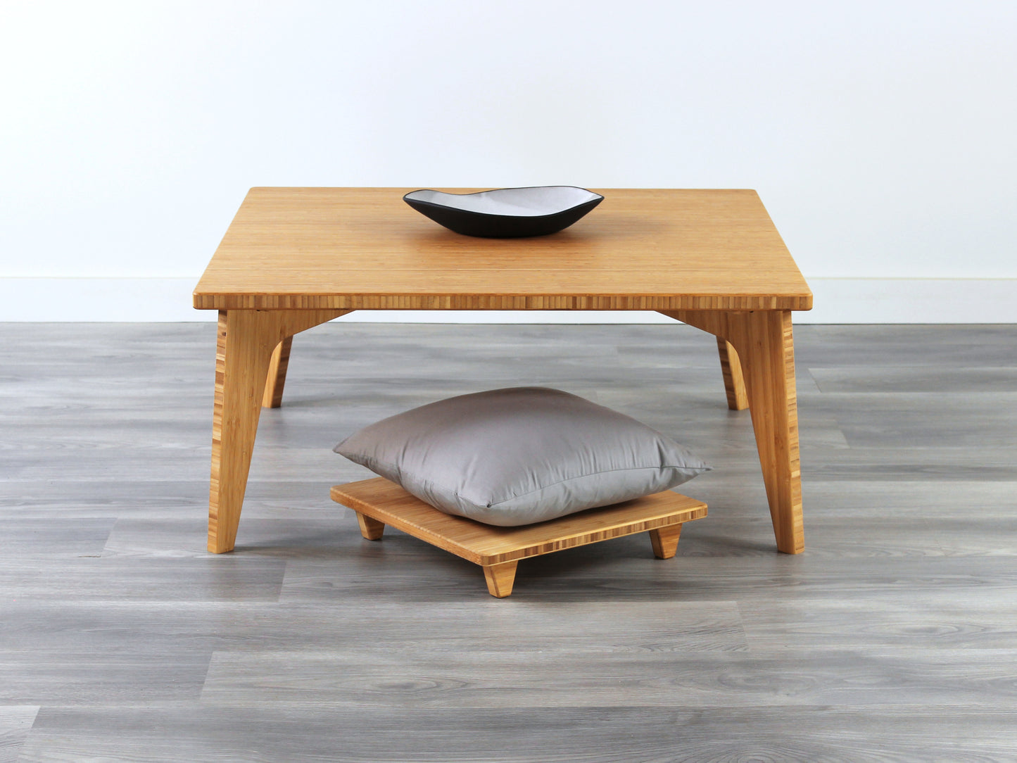 Small Square Table Set in natural finish. Floor Chair Posture with grey pillows are placed below. A small black pottery vessel is placed on top of the table. 

sustainable bamboo, renewable bamboo, solid bamboo, eco-friendly furniture, zero-waste, carbon neutral, natural materials, natural-based finish, repairable furniture