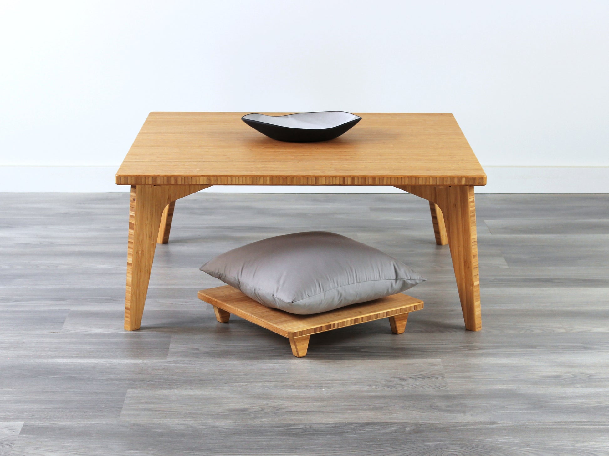 Small Square Table Set in natural finish. Floor Chair Posture with grey pillows are placed below. A small black pottery vessel is placed on top of the table. 

sustainable bamboo, renewable bamboo, solid bamboo, eco-friendly furniture, zero-waste, carbon neutral, natural materials, natural-based finish, repairable furniture