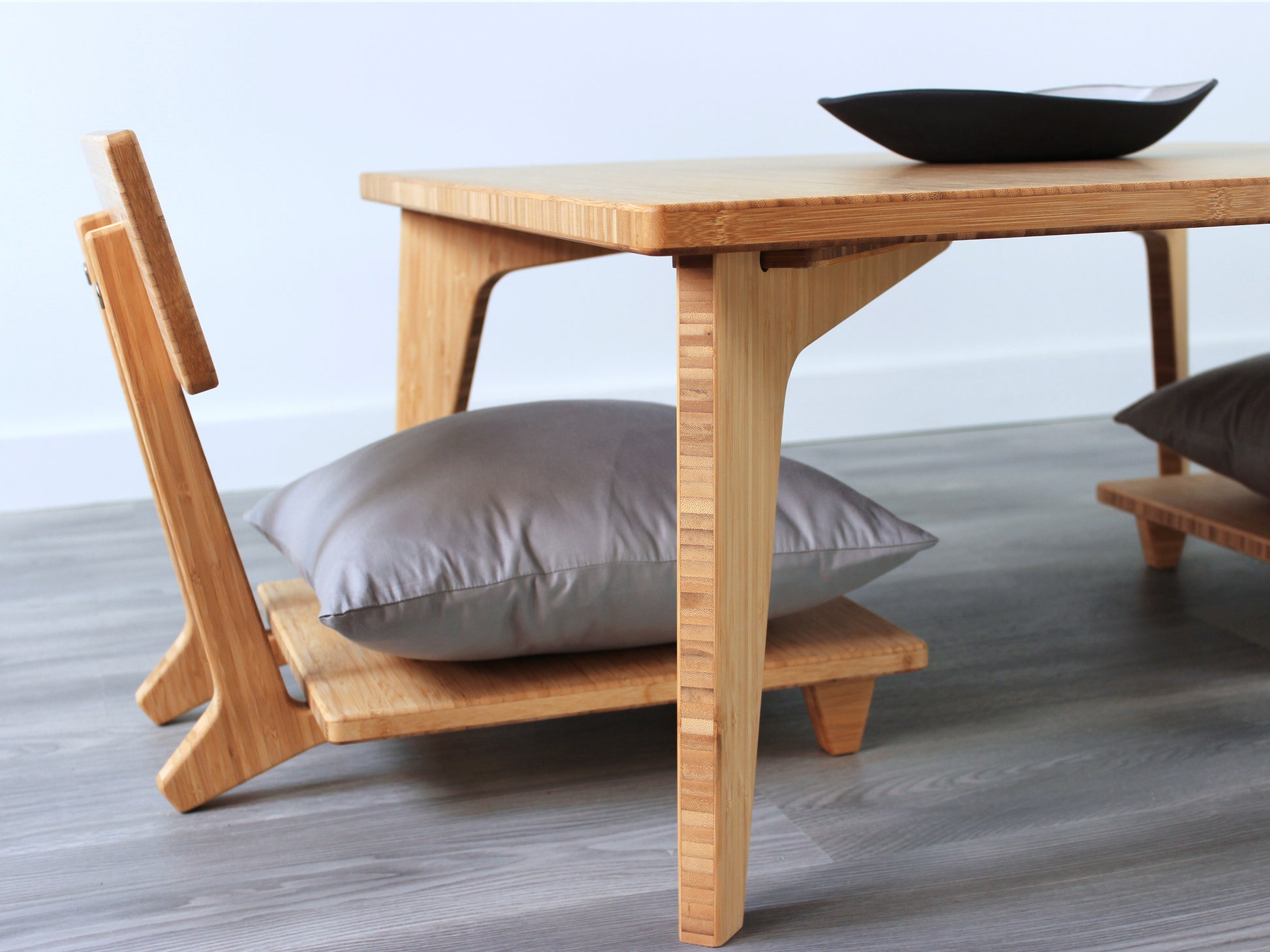 Small Square Table Set in natural finish. Two Floor Chair Comfort with grey pillows are placed below. A small black pottery vessel is placed on top of the table. 

sustainable bamboo, renewable bamboo, solid bamboo, eco-friendly furniture, zero-waste, carbon neutral, natural materials, natural-based finish, repairable furniture