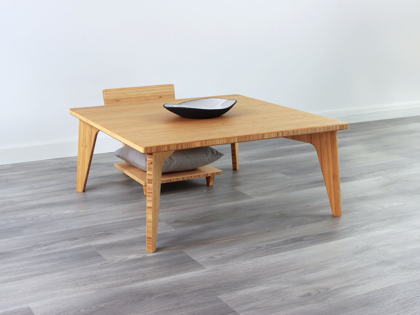 Small Square Table Set in natural finish. A Floor Chair Comfort with grey pillow is placed below. A small black pottery vessel is placed on top of the table. 

sustainable bamboo, renewable bamboo, solid bamboo, eco-friendly furniture, zero-waste, carbon neutral, natural materials, natural-based finish, repairable furniture