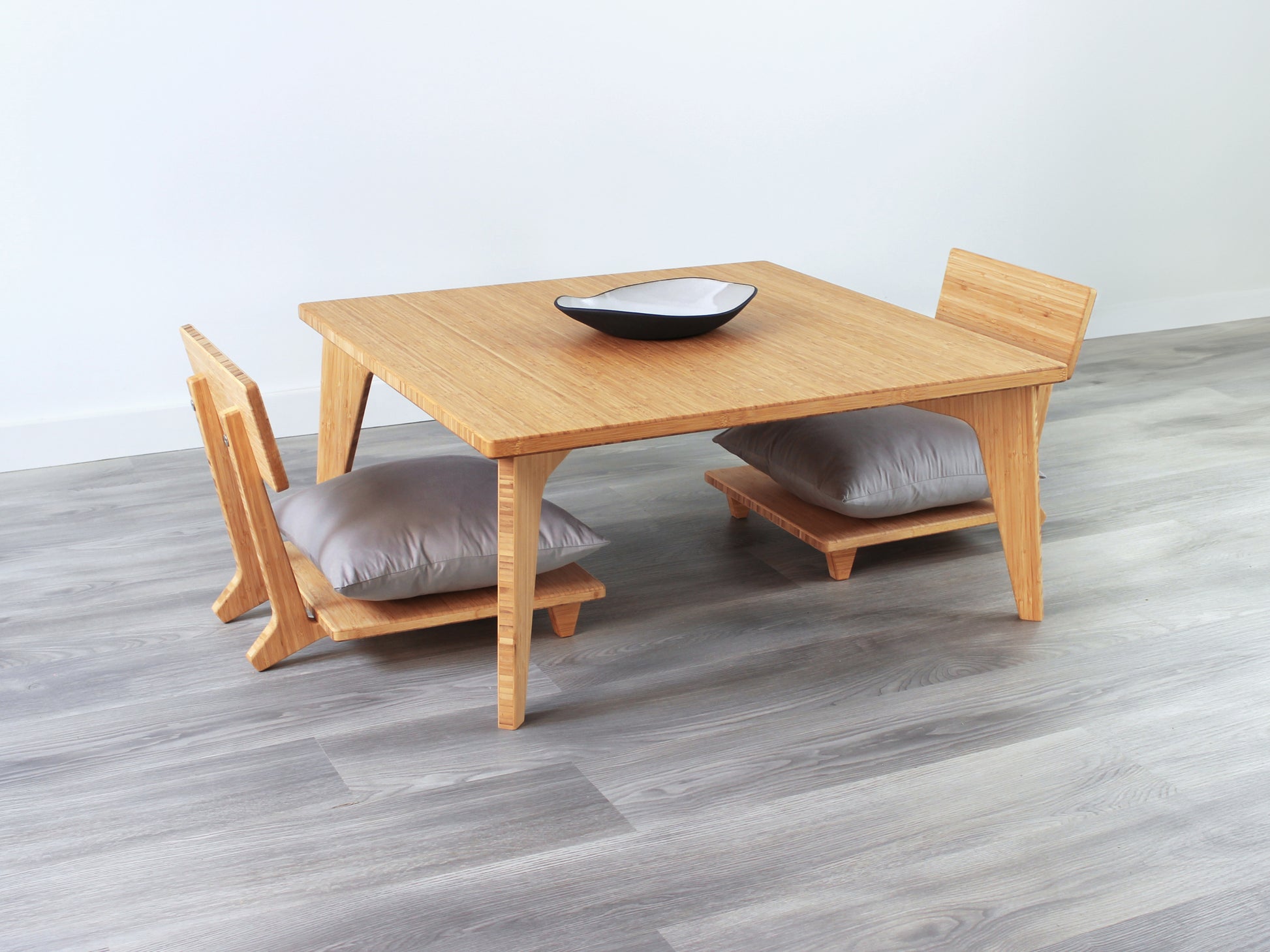 Small Square Table Set in natural finish. Two Floor Chair Comfort with grey pillows are placed below. A small black pottery vessel is placed on top of the table. 

sustainable bamboo, renewable bamboo, solid bamboo, eco-friendly furniture, zero-waste, carbon neutral, natural materials, natural-based finish, repairable furniture