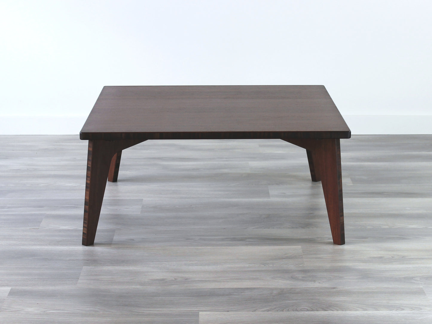 A small square, walnut bamboo table with visible wood grain, placed on a grey floor.