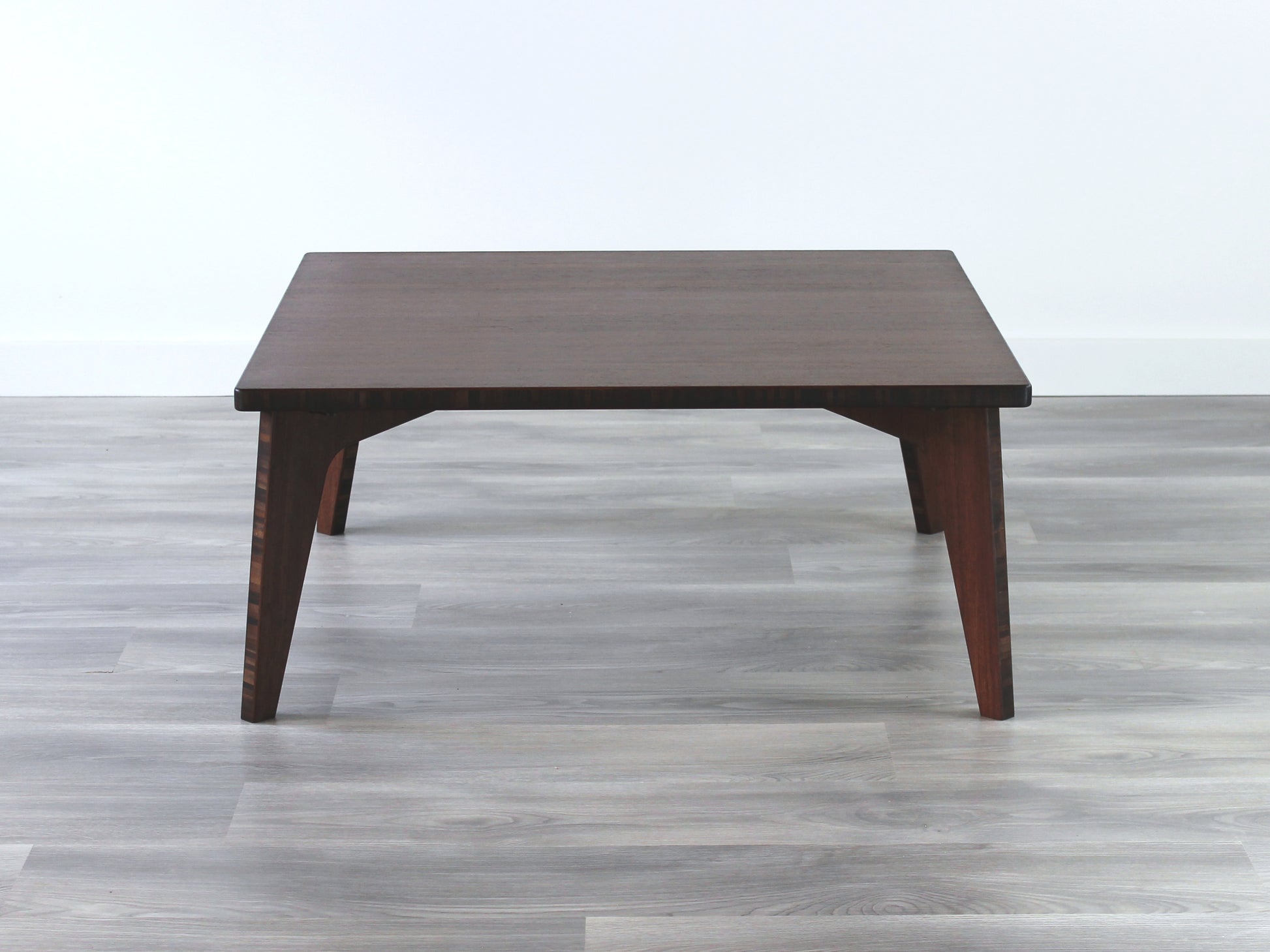 A small square, walnut bamboo table with visible wood grain, placed on a grey floor.