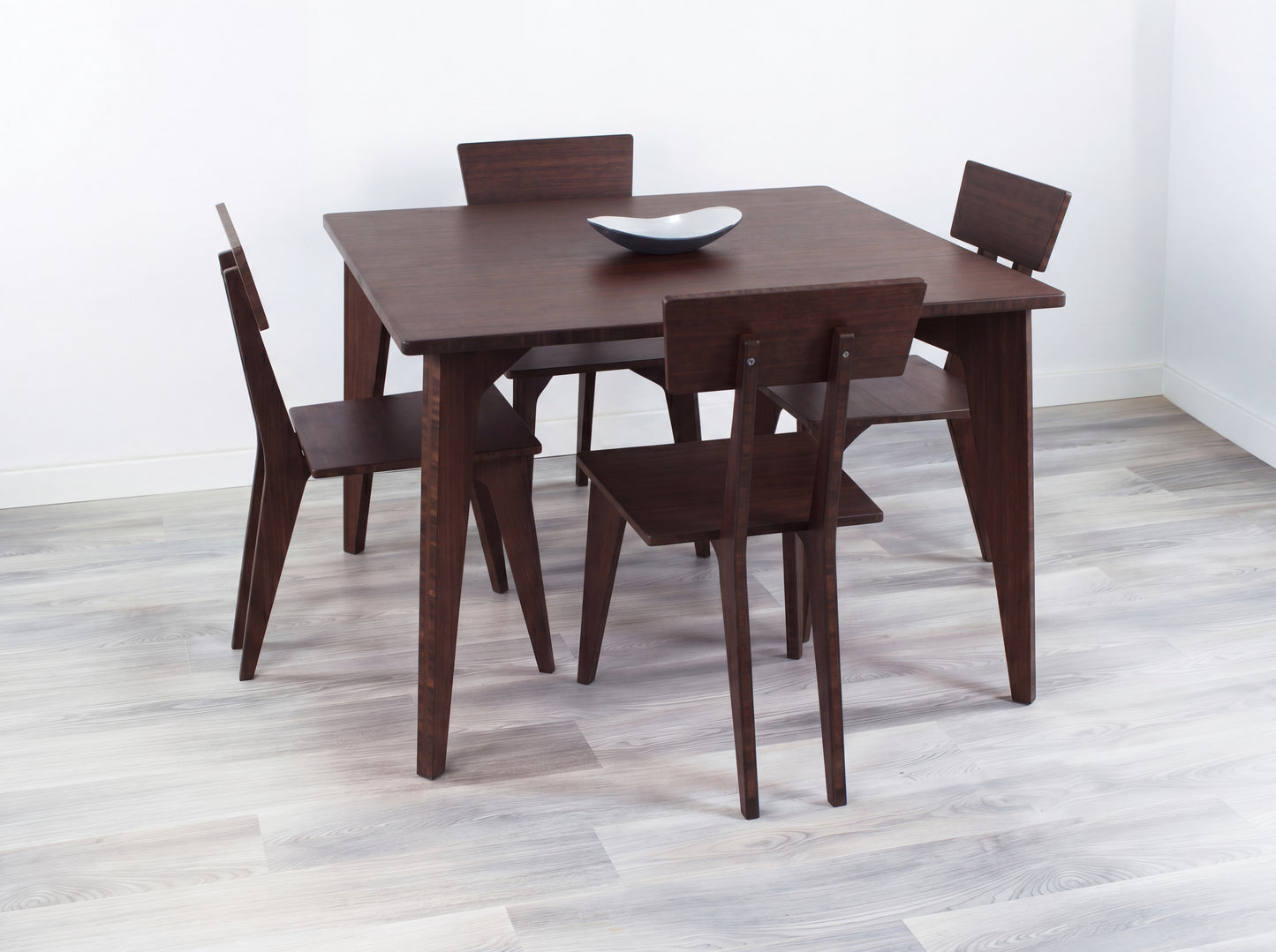 Bamboo dining table set with four chairs on a light wooden floor against a white wall.