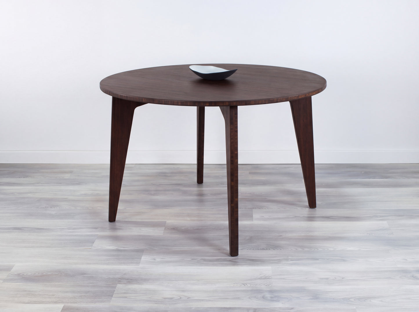 Round bamboo table on a gray floor with a white wall background