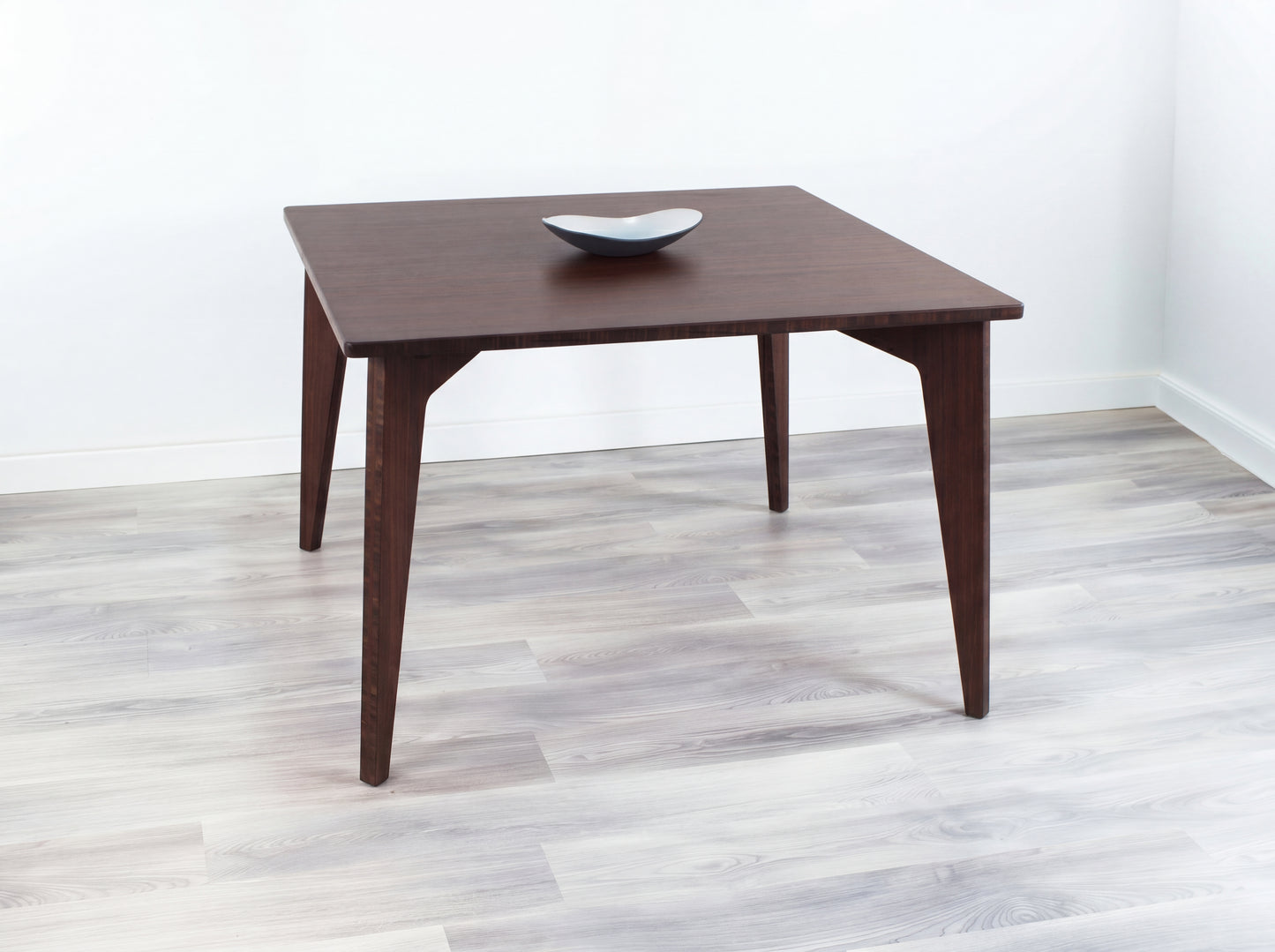 Bamboo table with a white bowl on a light wooden floor and white wall background