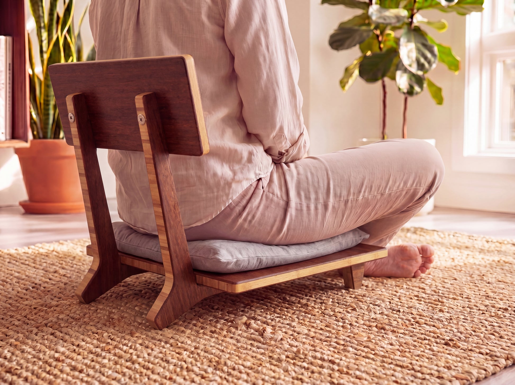 Person sitting on a bamboo meditation chair with cushions in a bright room.

